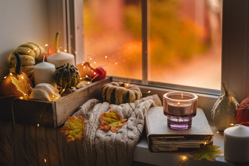 mini pumpkins and gourds on a white knit blanket, next to a book with a candle, showing a cozy setting